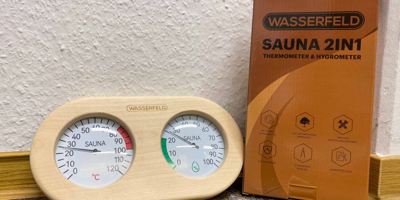 Saunathermometer und Verpackung samt Schraube und Mini-Schraubendreher auf dem Boden.