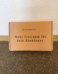 Geschlossener Verpackungskarton mit Schriftzug "Mehr Freiraum für dein Abenteuer" darauf.