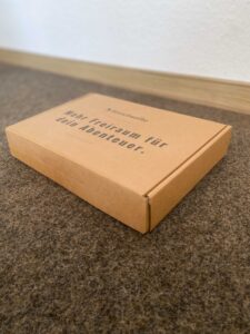 Geschlossener Verpackungskarton mit Schriftzug "Mehr Freiraum für dein Abenteuer" darauf.