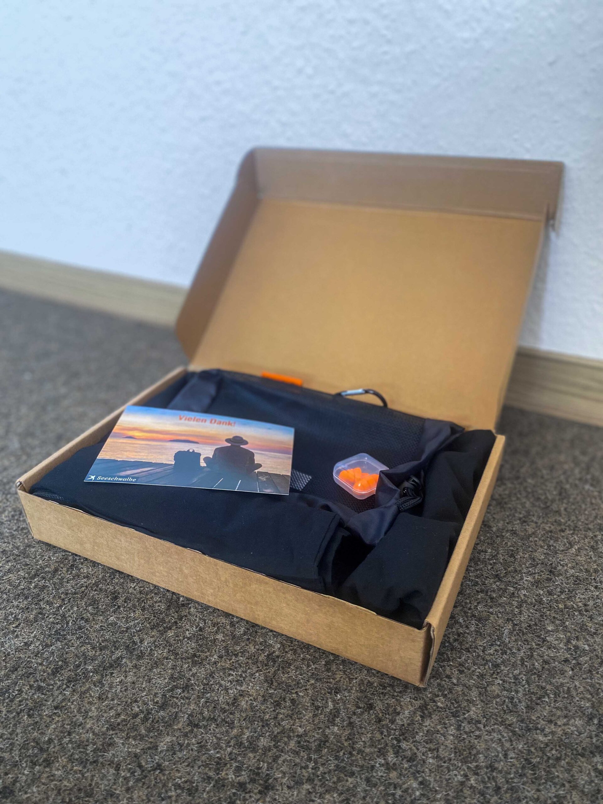 Hüttenschlafsack mit Beutel, Ohrenstöpseln Karte im Verpackungskarton seitlich von vorne.