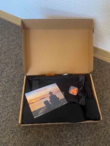 Hüttenschlafsack mit Beutel, Ohrenstöpseln Karte daraufliegend im Verpackungskarton.