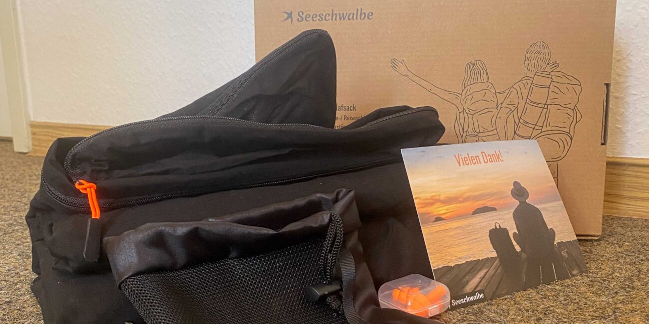 Hüttenschlafsack, Beutel, Ohrstöpsel, Dankeskarte und Verpackung aller zusammen neben- und hintereinander aufgestellt.