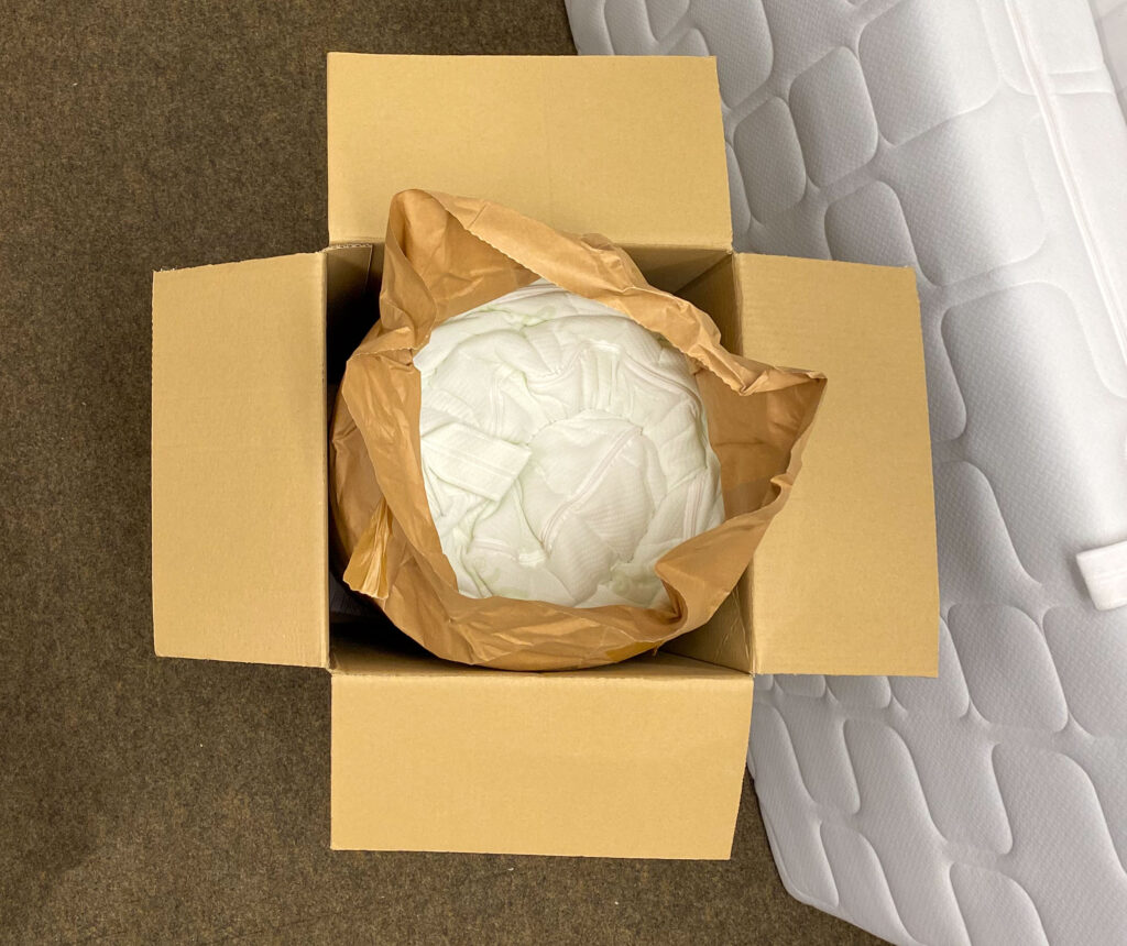 Active Greenfirst Matratze von oben eingerollt im Karton mit geöffneter Papierfolie.