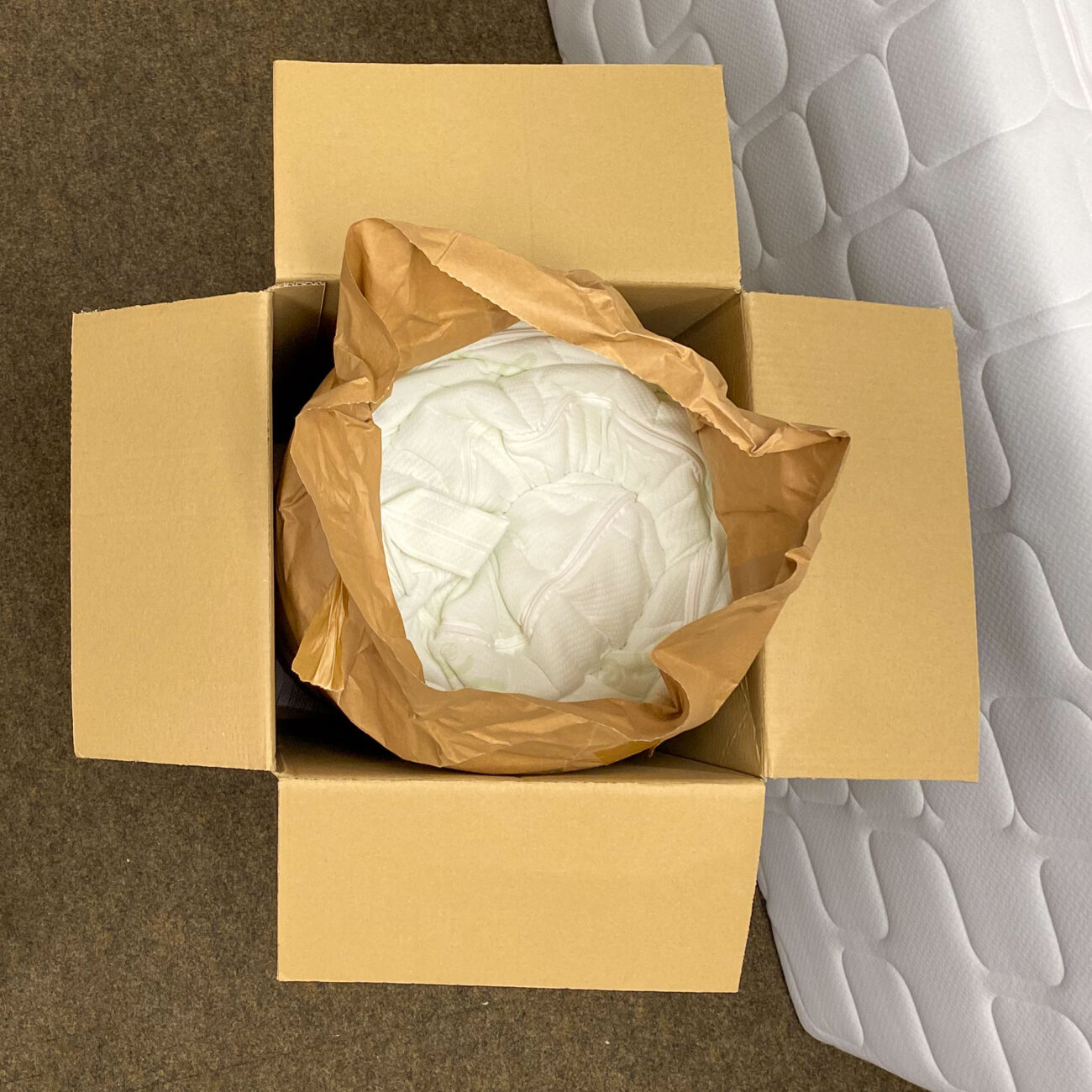 Active Greenfirst Matratze von oben eingerollt im Karton mit geöffneter Papierfolie.